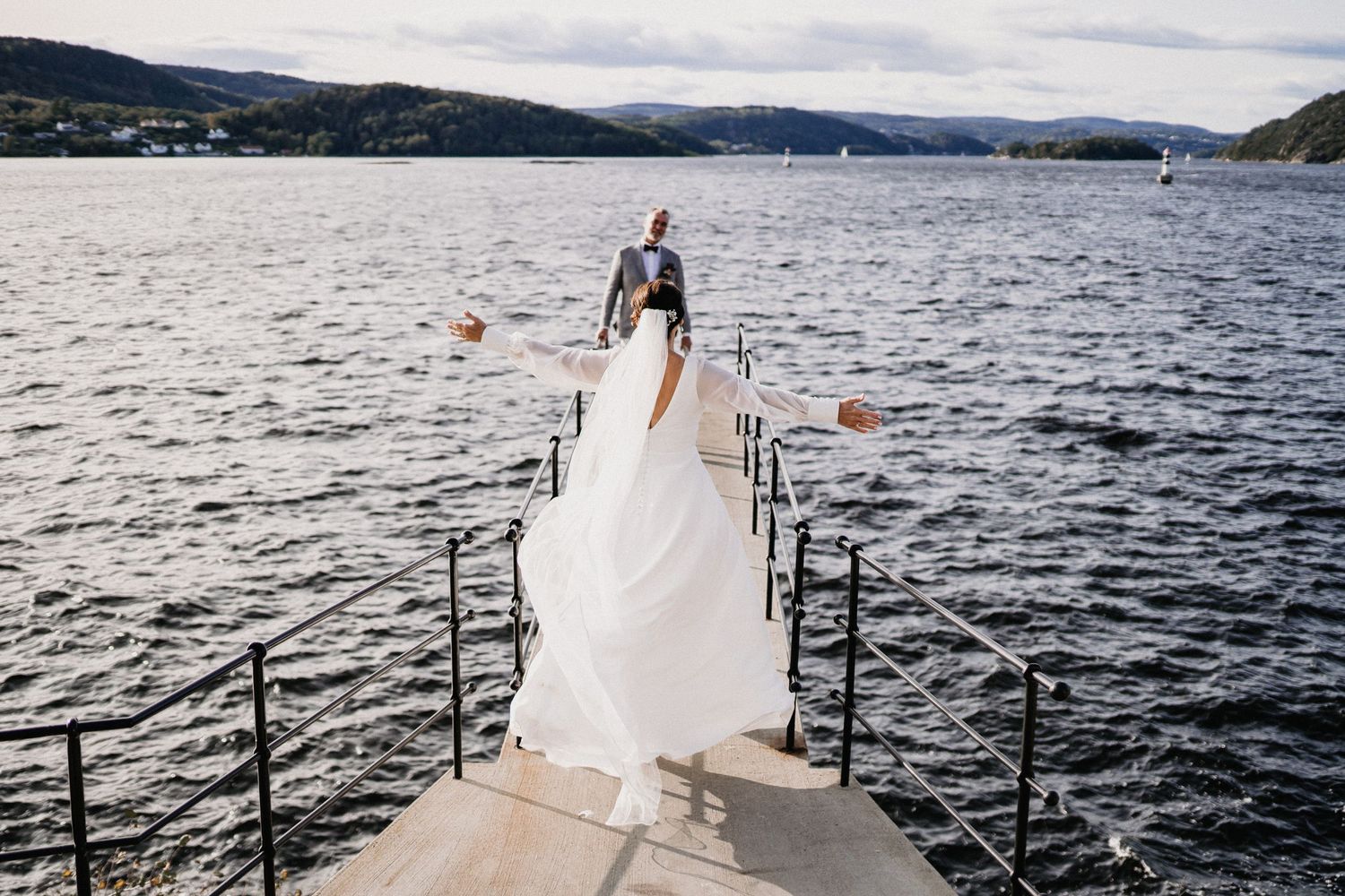 Wedding couple on a dock overlooking a scenic lake with mountains in the background.