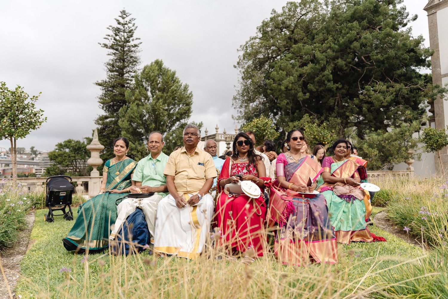 Large wedding party poses for outdoor group photo on grassy hillside.