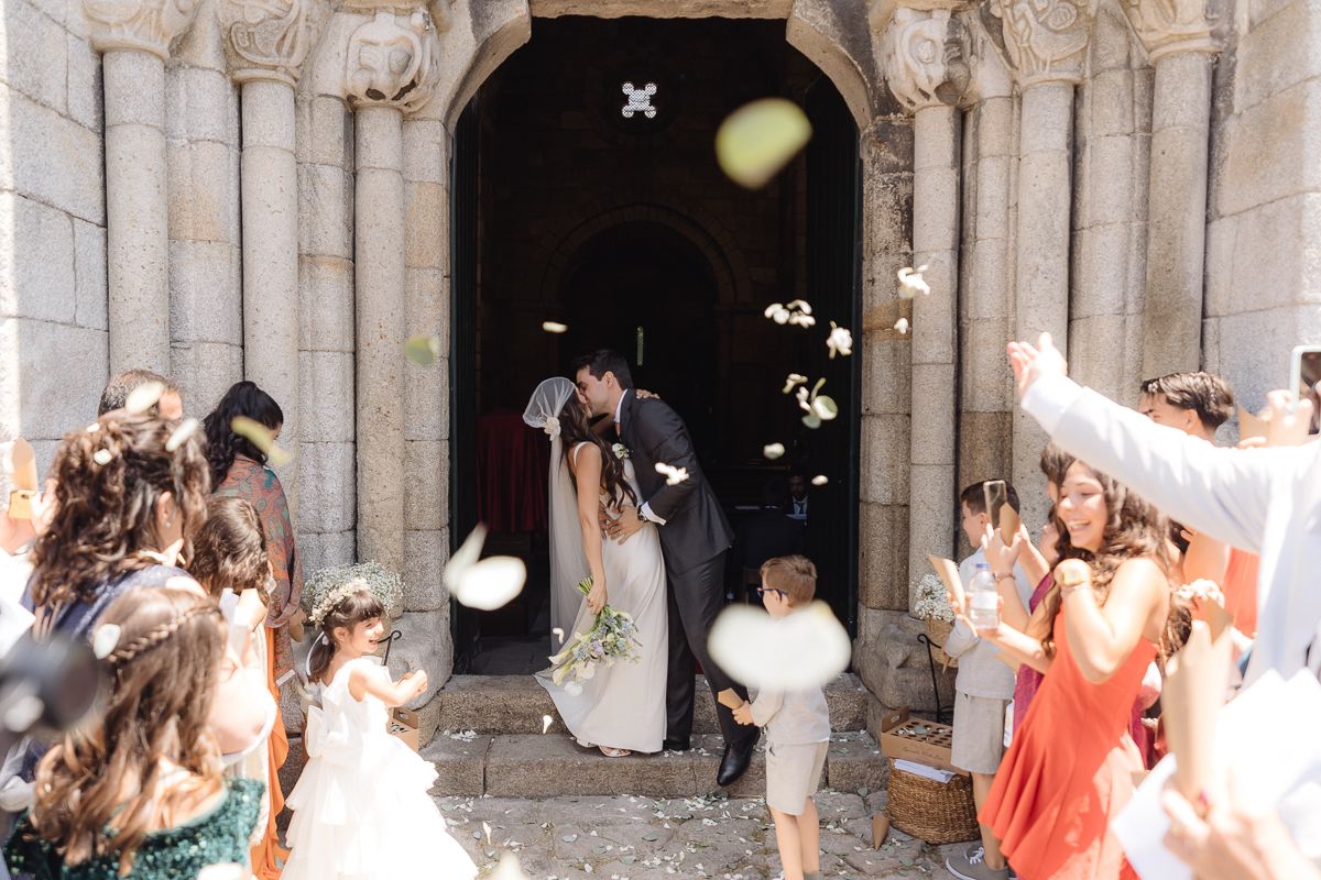 Stone church archway frames wedding celebration with guests throwing petals.