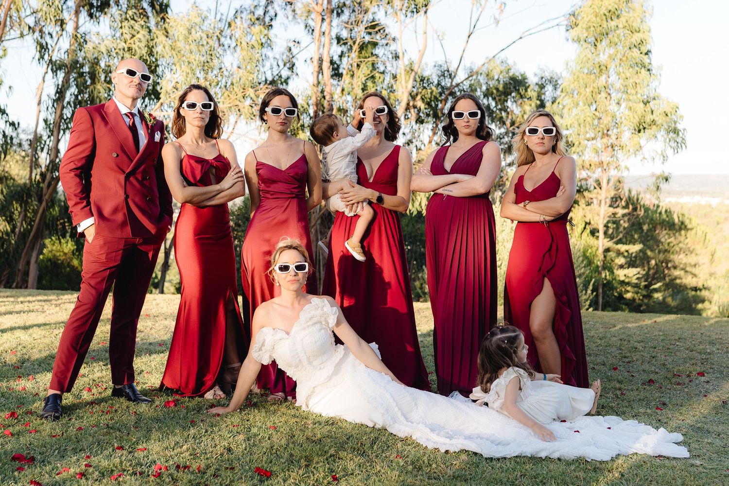 Wedding party in coordinated burgundy attire posing together outdoors.