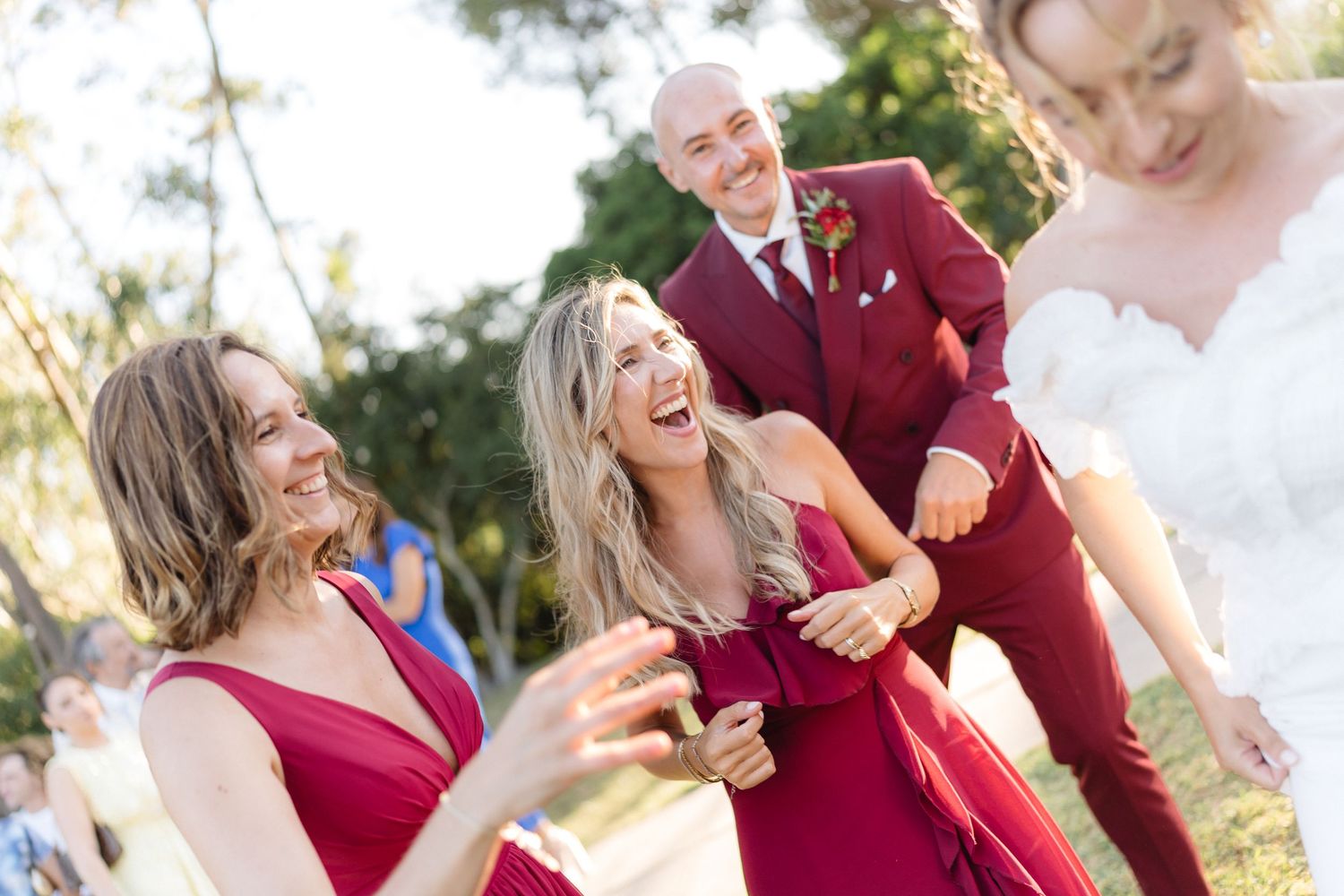 Wedding celebration with attendees in burgundy and white attire laughing joyfully outdoors.