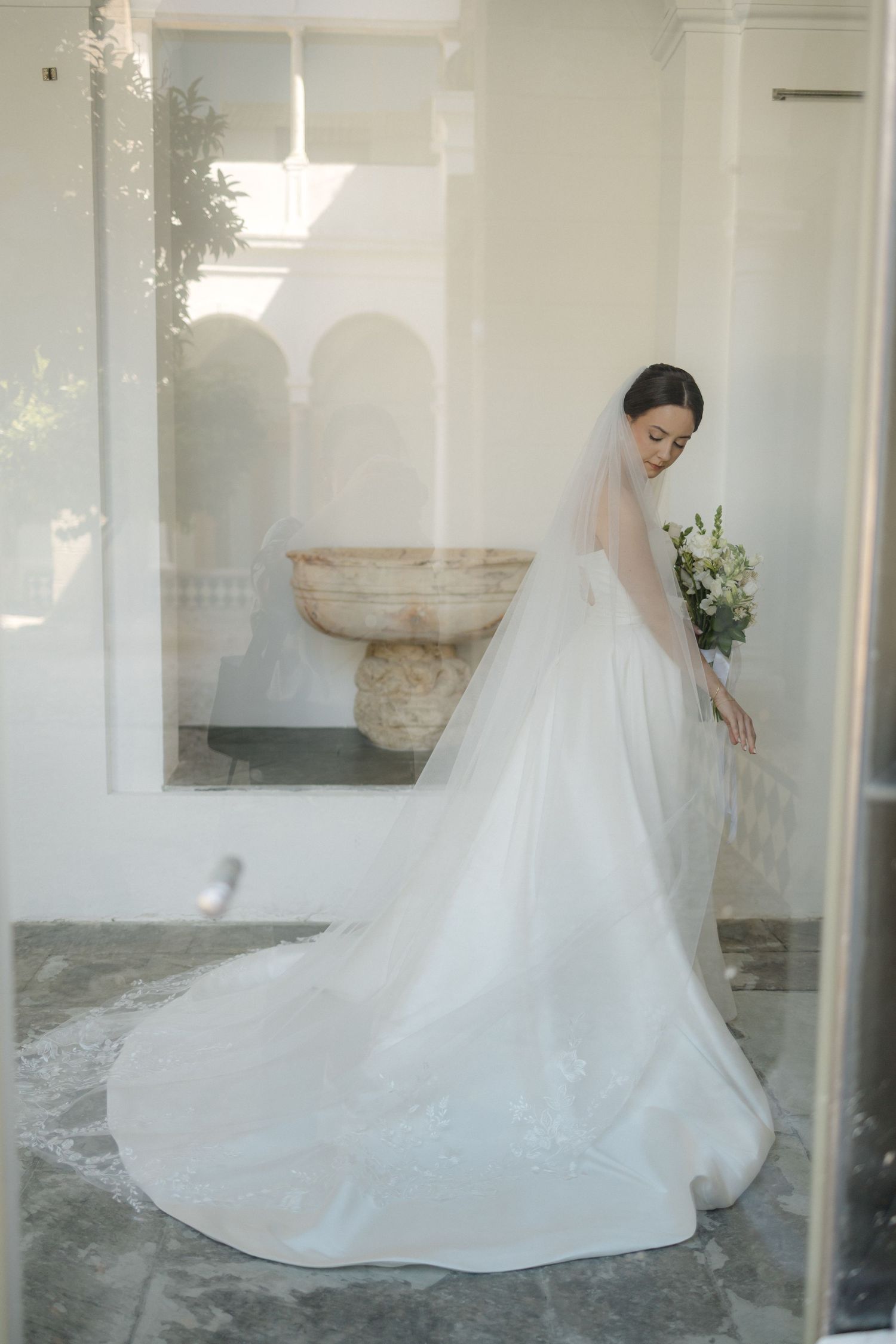 Elegant white wedding dress with long train photographed in a bright interior space.