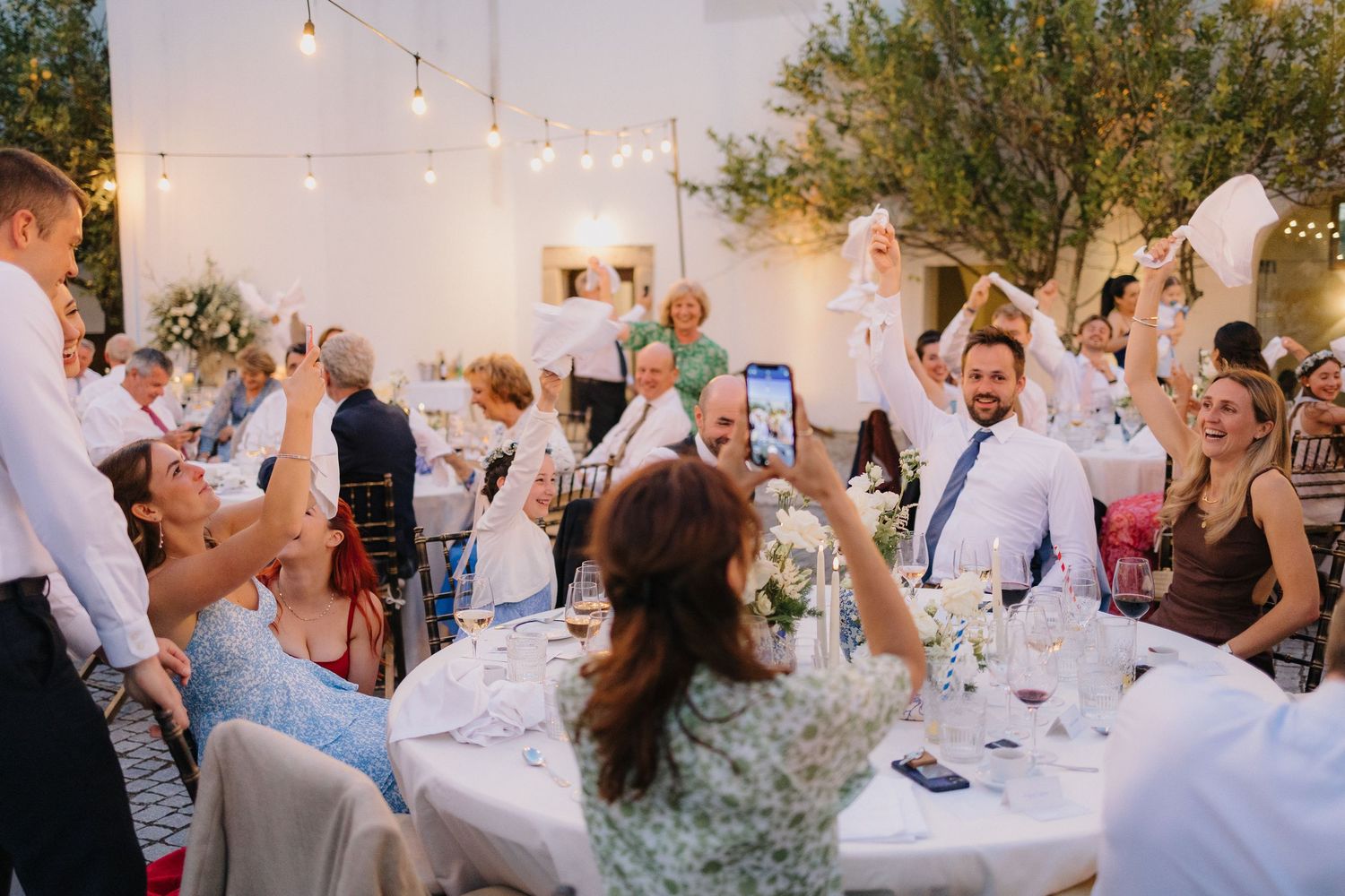 Guests celebrating and raising their hands during an outdoor evening reception.