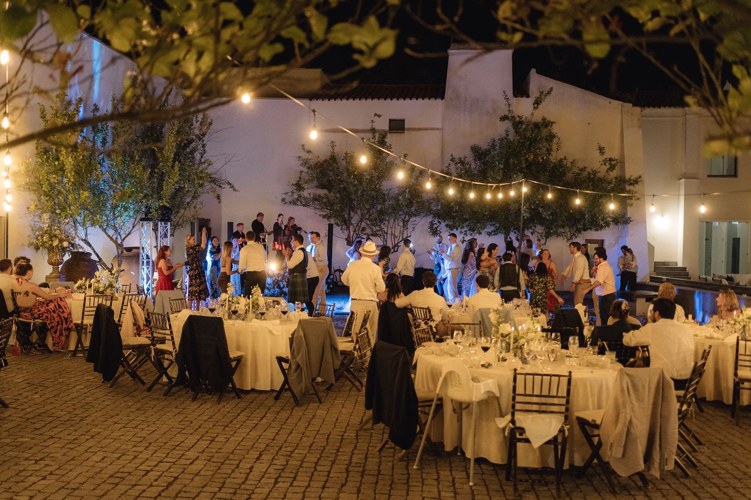 Outdoor wedding reception venue decorated with string lights and white table settings.