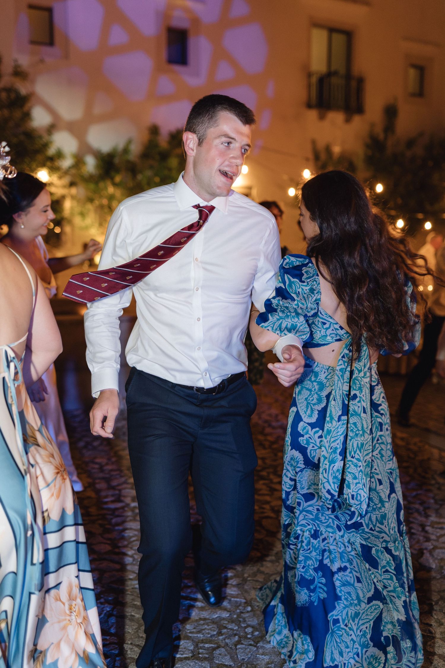 Wedding guests dancing and celebrating on a cobblestone patio at night.