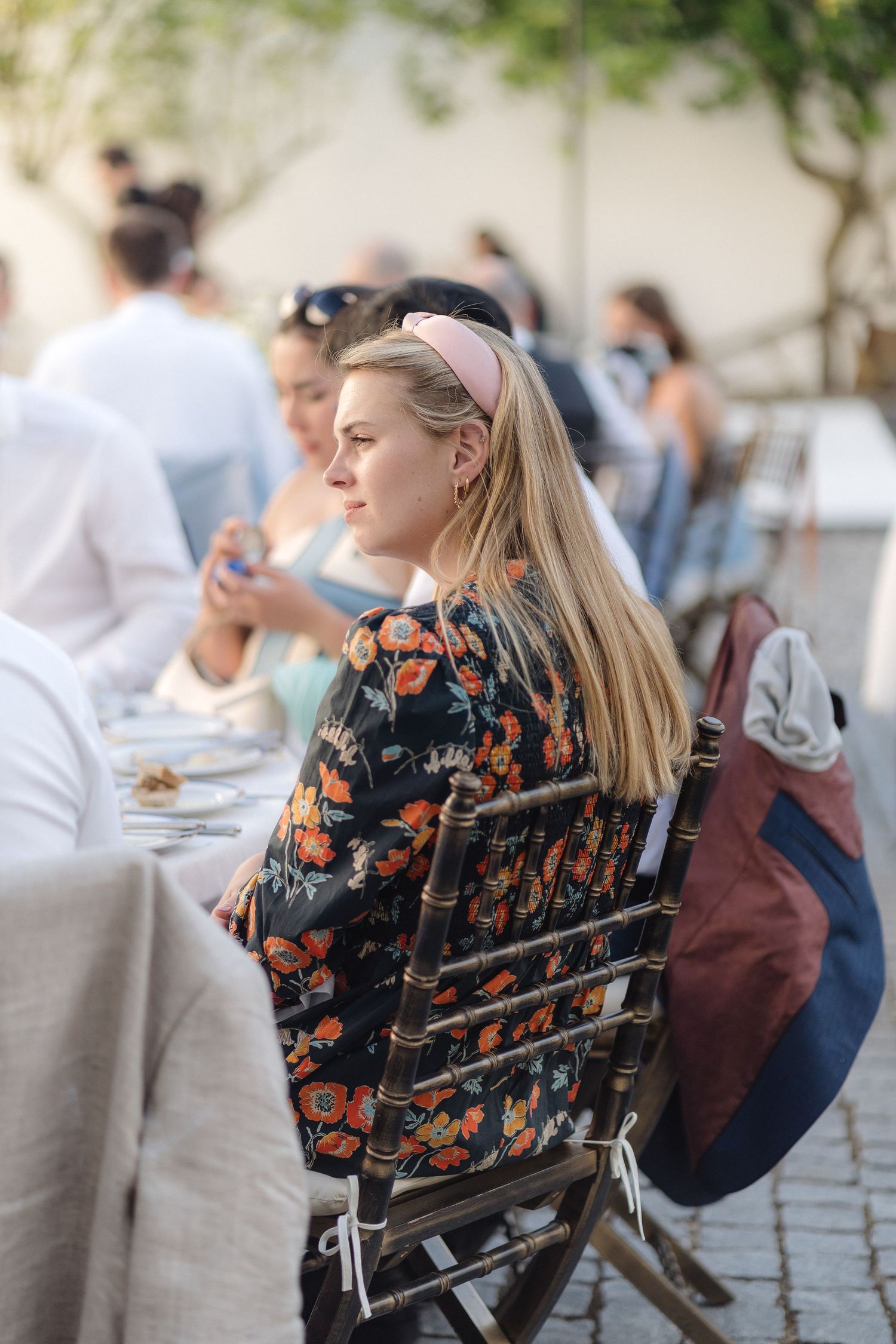 Guest in floral dress seated at outdoor dining table during elegant reception.