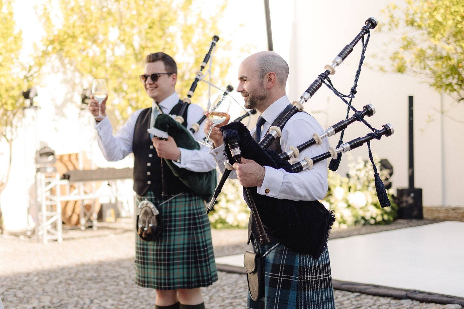 Bagpipers in traditional Scottish kilts performing at an outdoor wedding celebration.