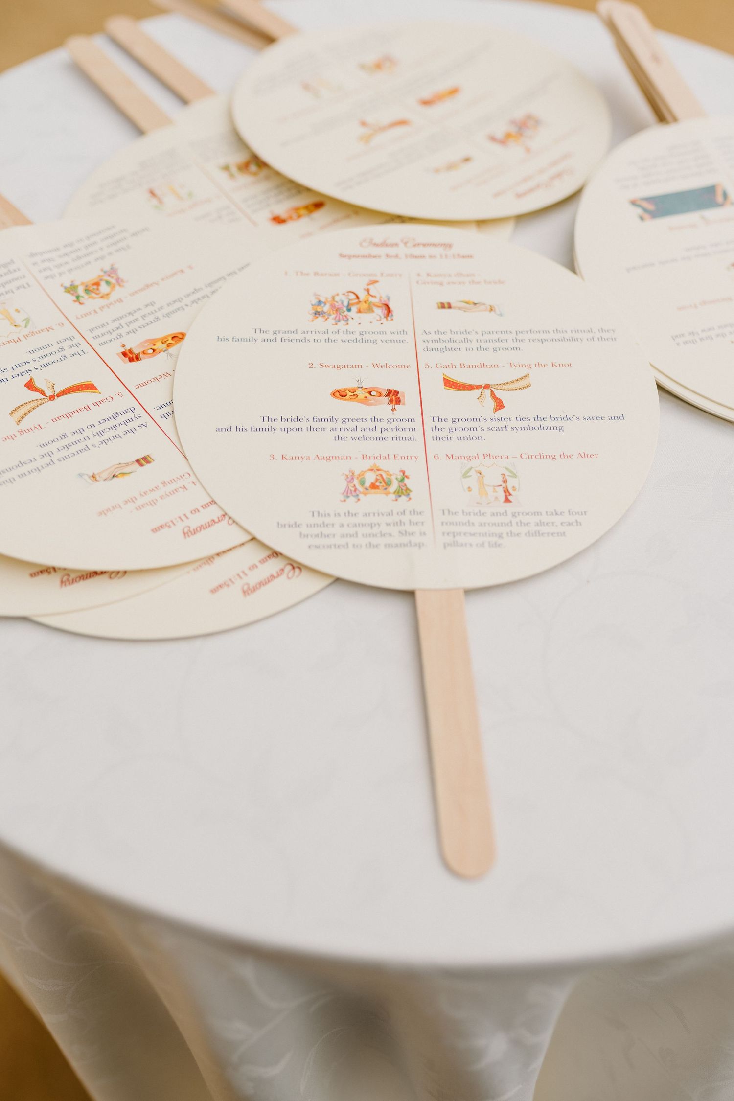 Wedding program fans with illustrated instructions laid out on a white tablecloth.