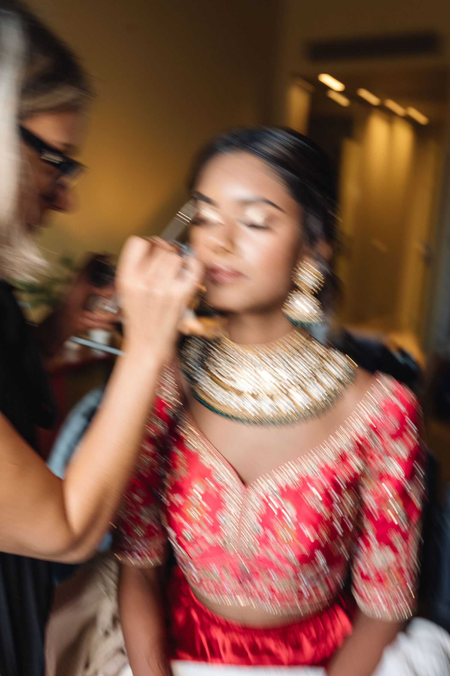 Motion blur photo of makeup application in traditional red and gold wedding attire.
