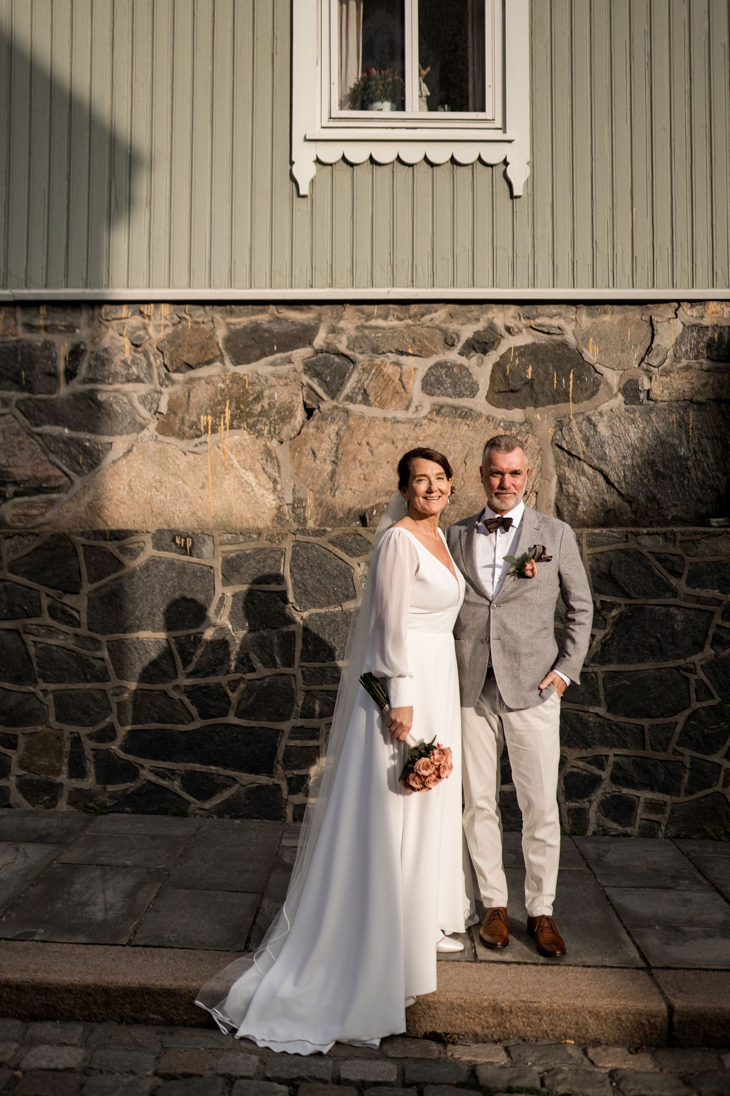 Wedding portraits against a rustic stone wall and grey building exterior.