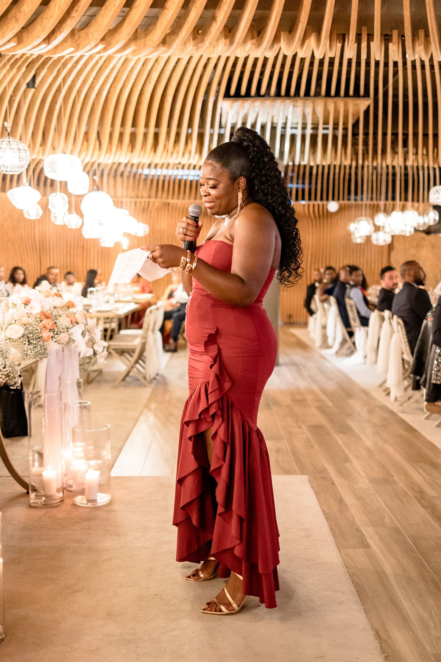 Wedding reception in a rustic wooden barn venue with dramatic curved ceiling beams and string lights.