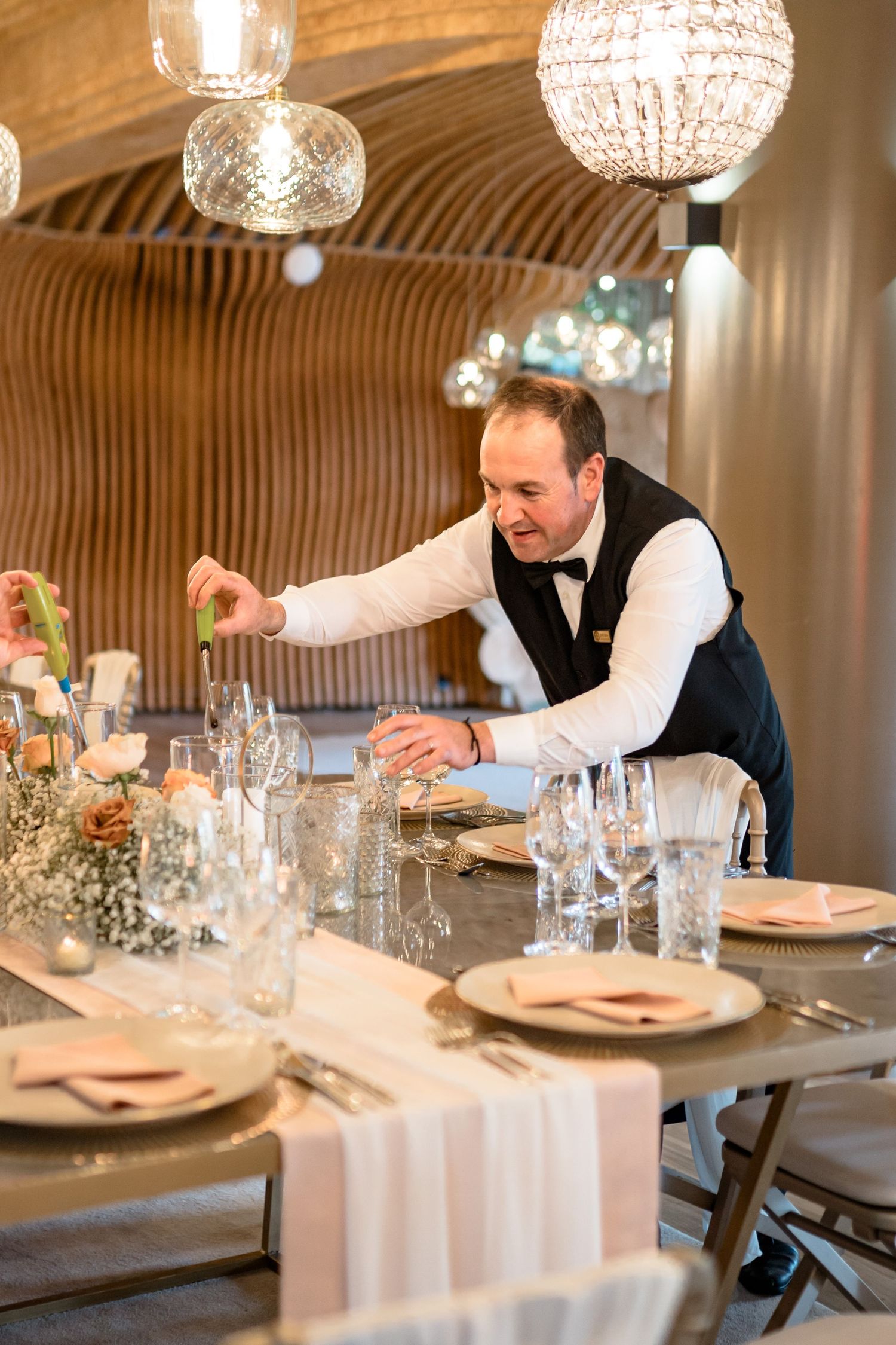 Server setting an elegant dining table with crystal glassware and fine dinnerware.