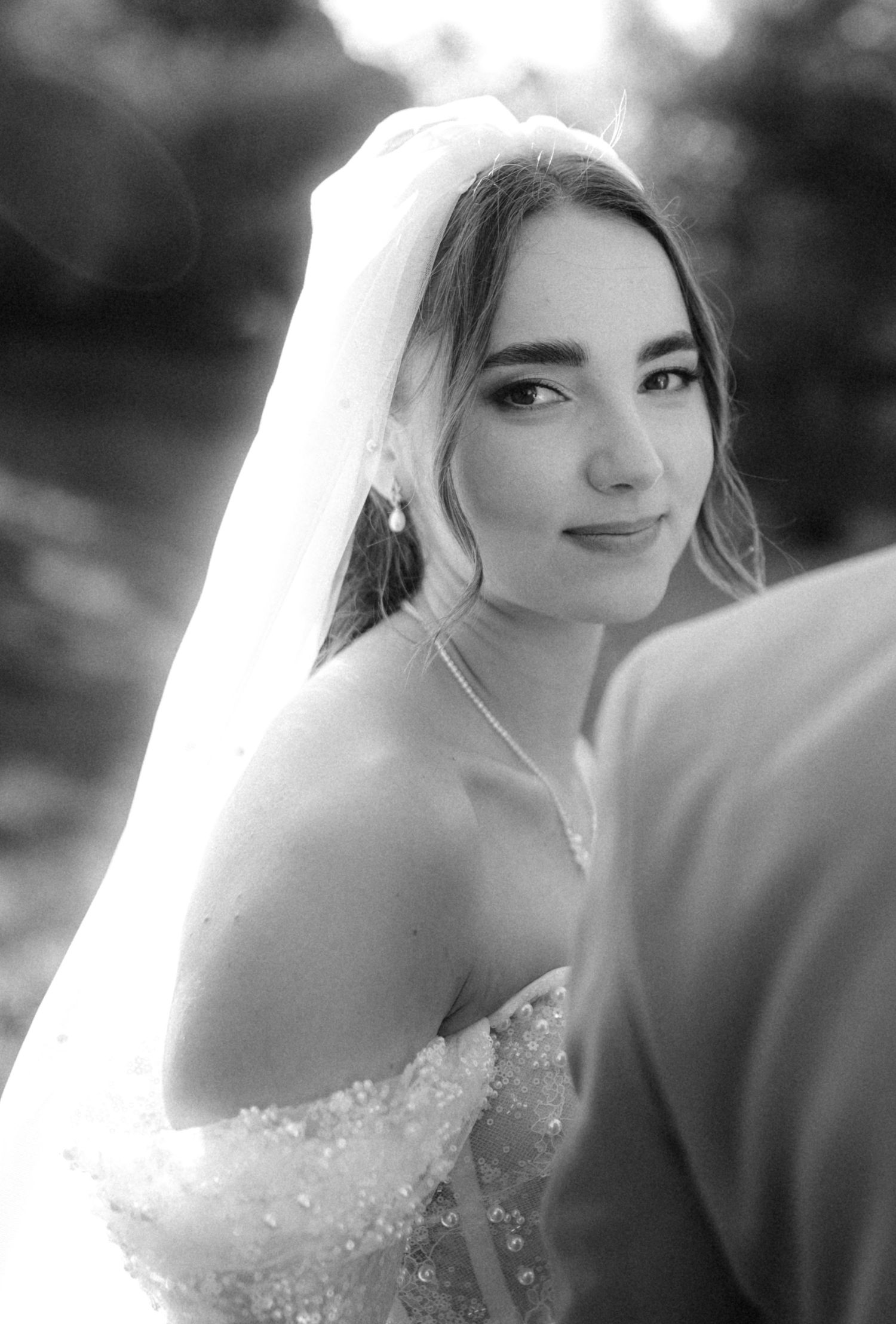 Elegant bridal portrait showcasing detailed bodice and veil in soft black and white.