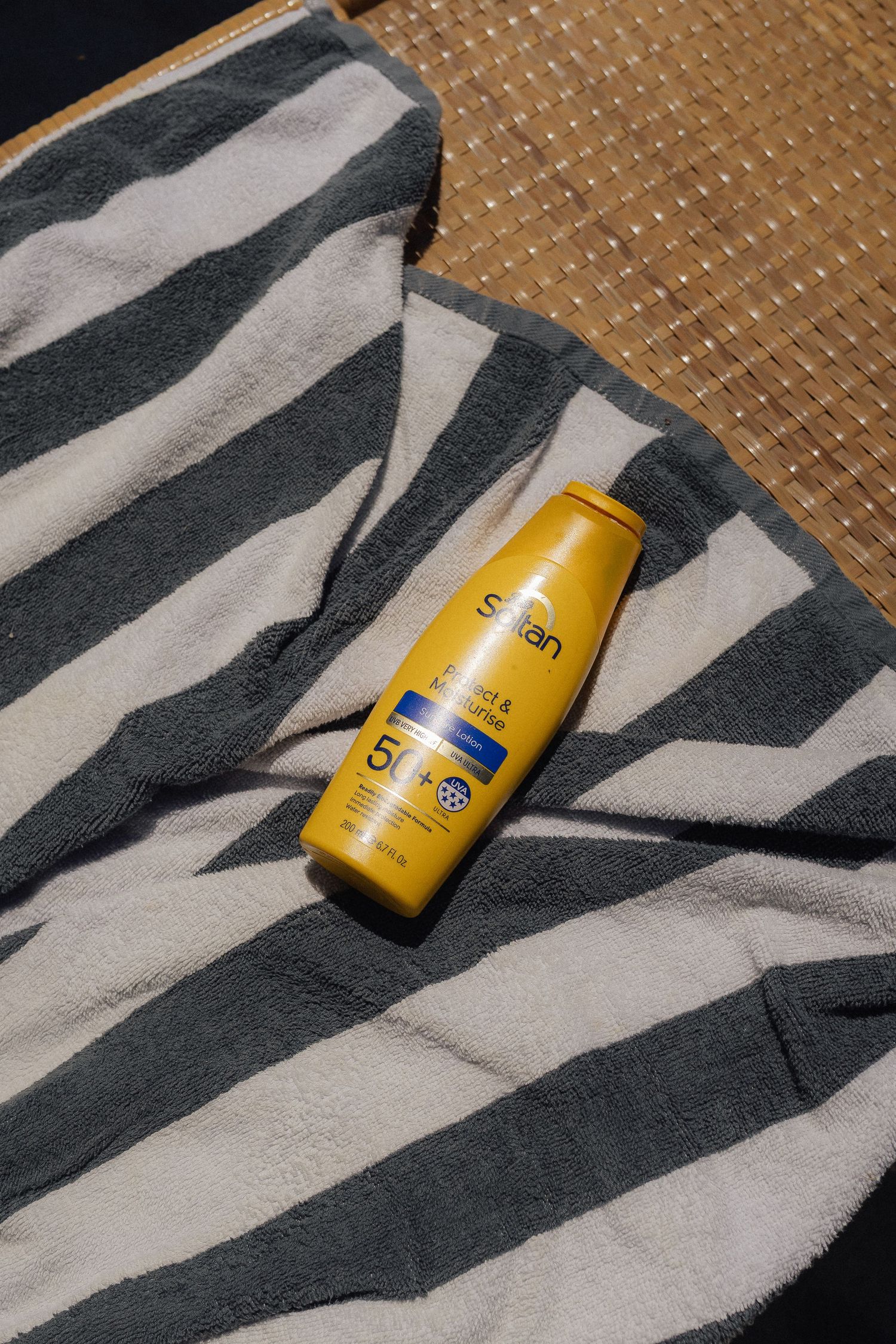 Yellow sunscreen bottle on striped beach towel against woven surface.