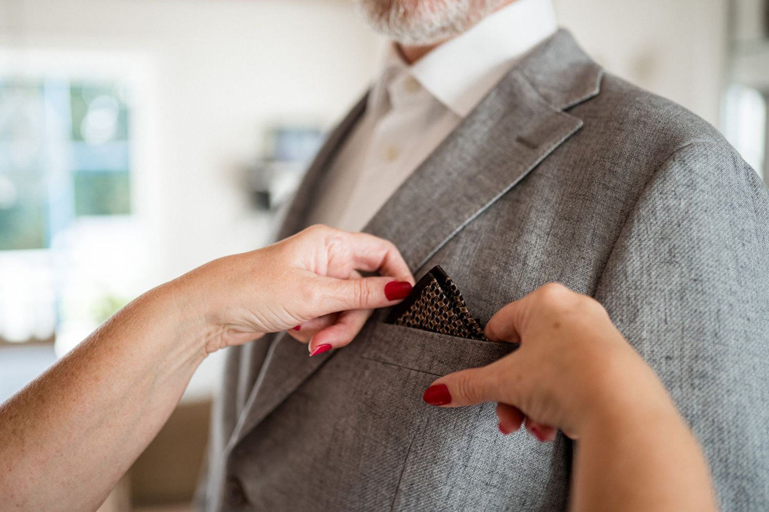 Close-up of hands adjusting a grey suit lapel and collar against a light background.