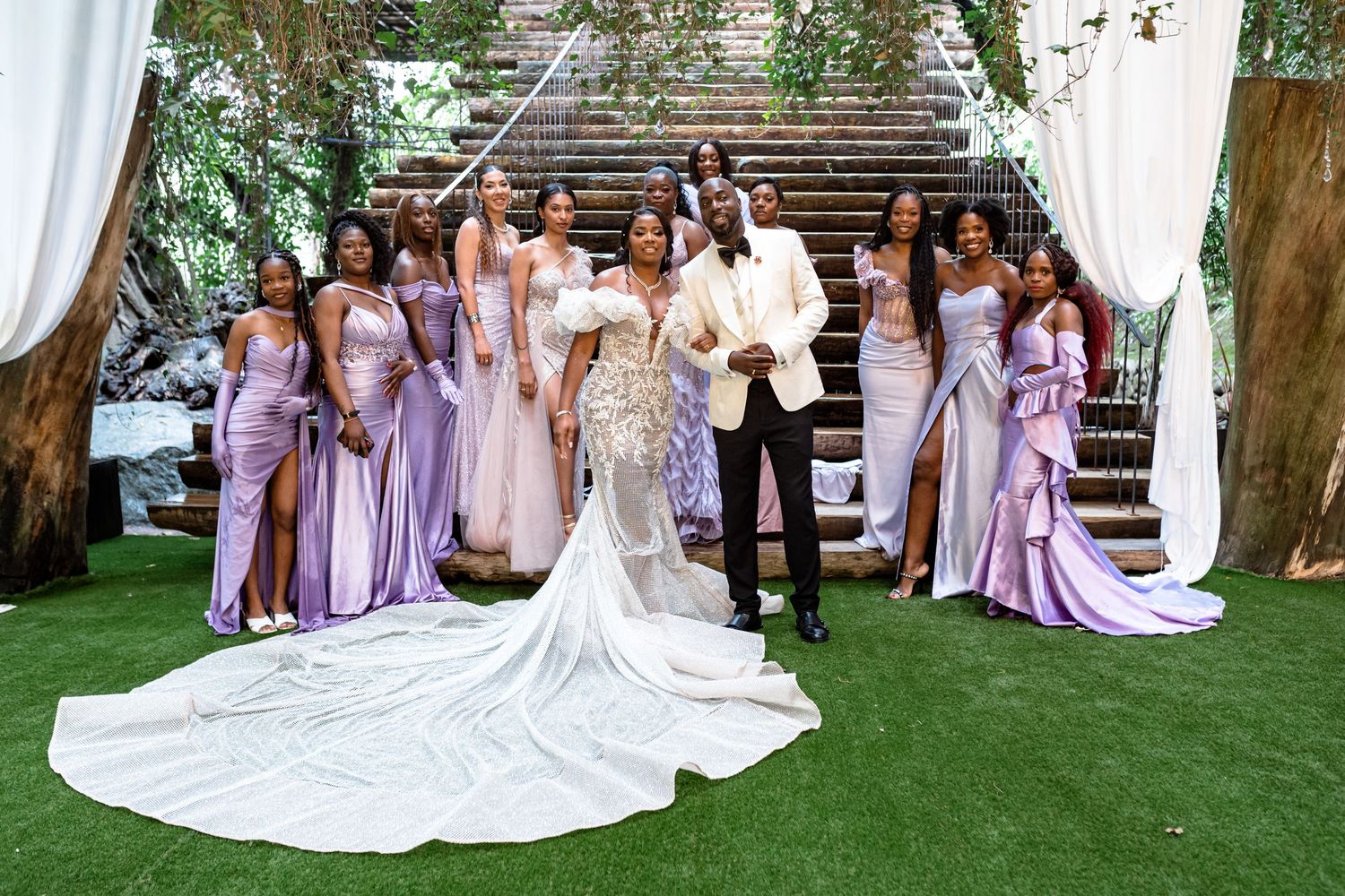 Wedding party members in lavender dresses pose with the bride on a manicured lawn.