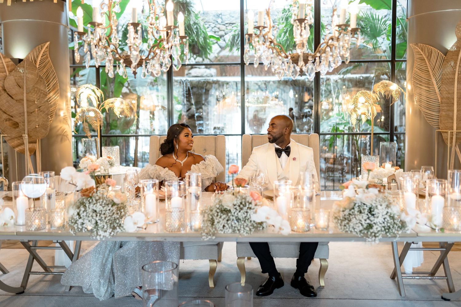 Wedding reception tables decorated with crystal chandeliers and elegant white floral centerpieces.