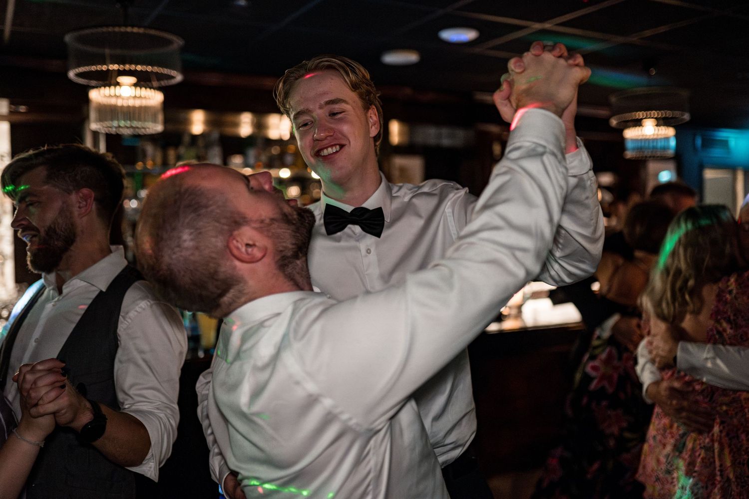 Wedding guests dancing and celebrating at a dimly lit reception venue.