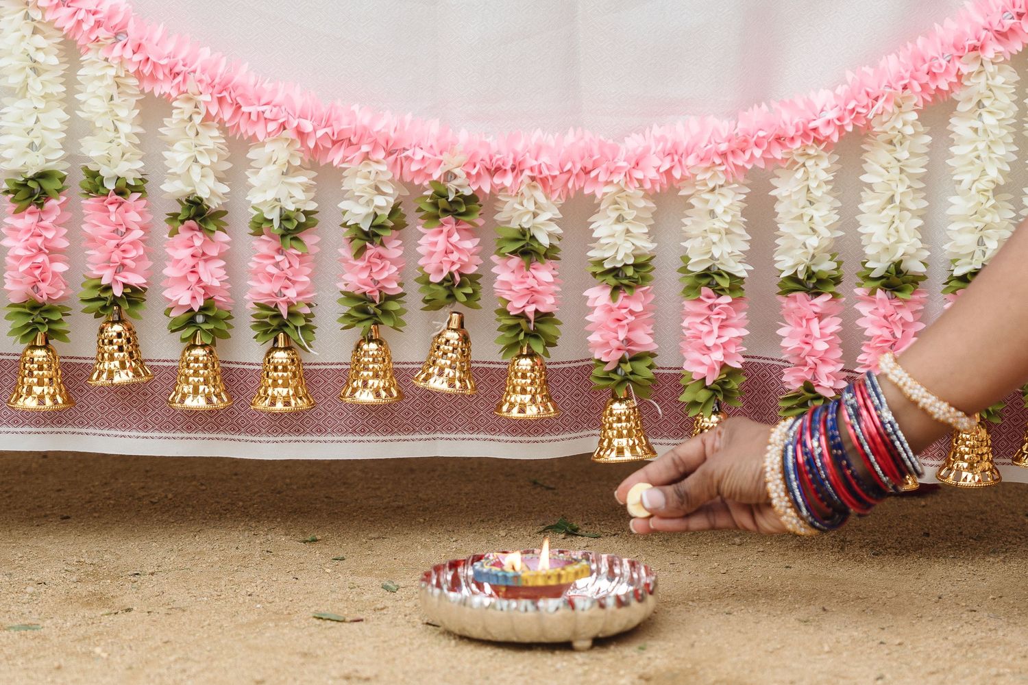 Pink and white floral decorations with hanging bells creating an elegant wedding ceremony border.