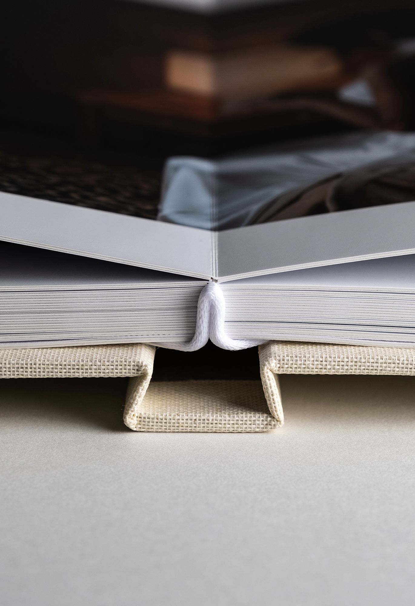 Close-up view of an open book spine showing white binding and beige linen cover details against a light background.