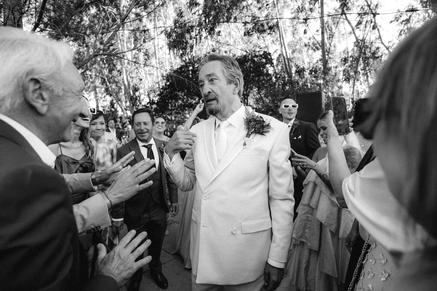 Black and white photo of wedding guests dancing and celebrating at an outdoor reception.