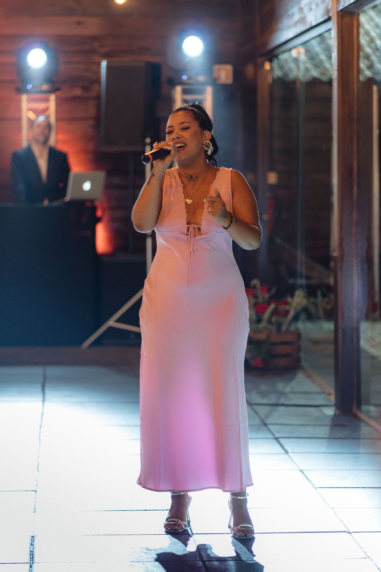 A performer in a long pink dress sings passionately on stage with dramatic lighting in the background.