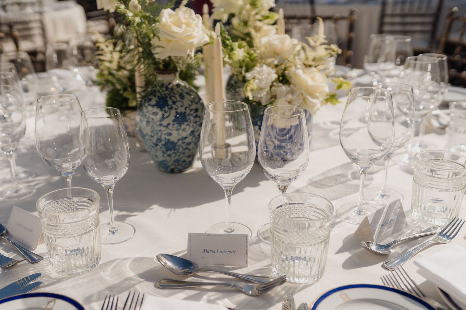 Wedding reception table decorated with blue and white vases, white flowers, and crystal place settings.