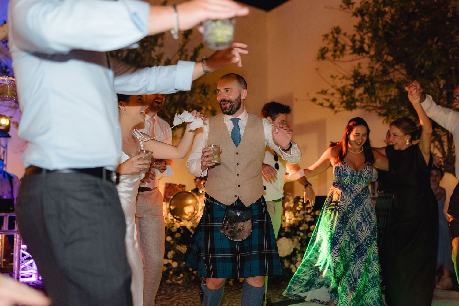 Wedding guests dancing and celebrating under decorative lighting at an outdoor reception.