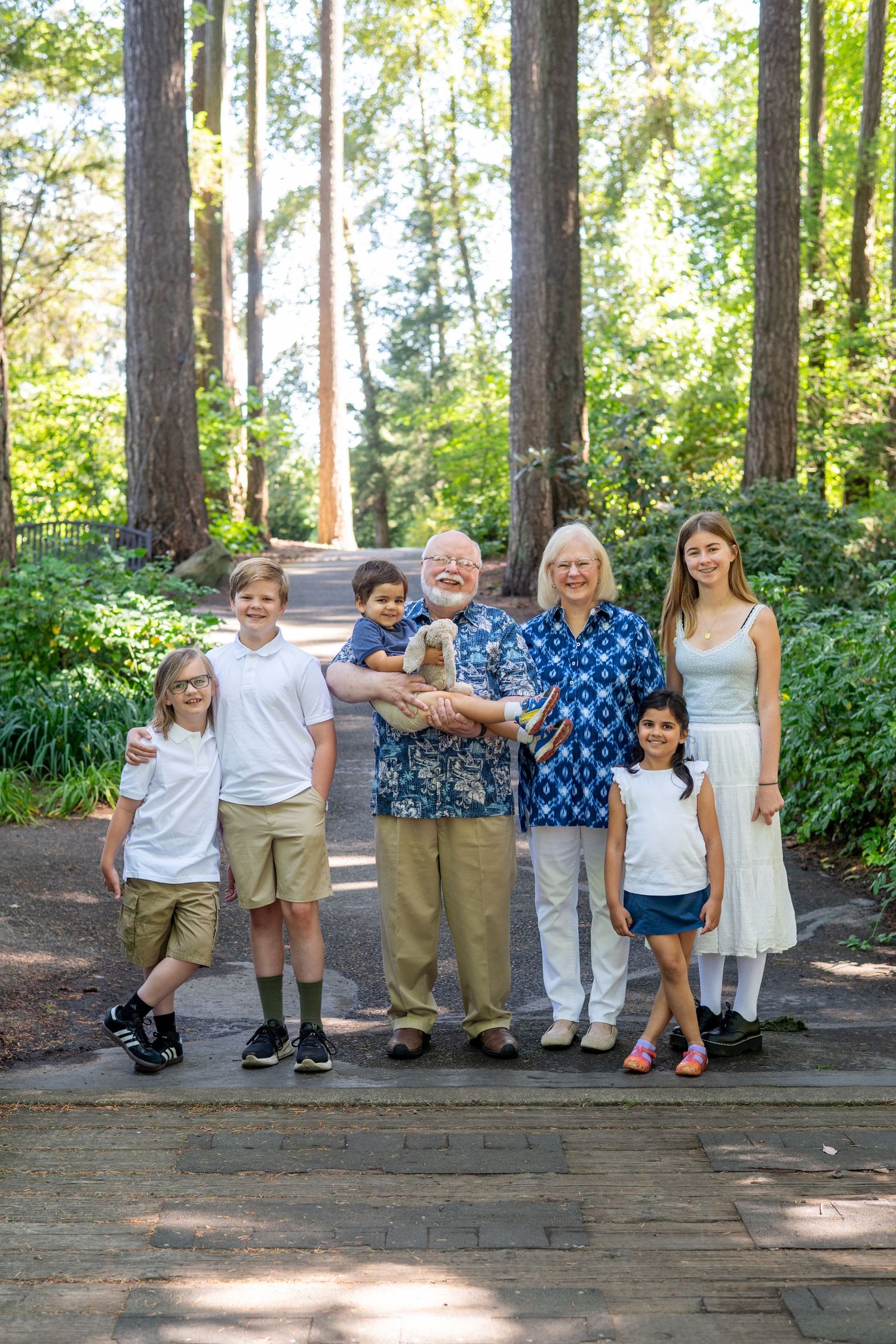 A group of people standing together outdoors in a wooded area with tall pine trees in the background.