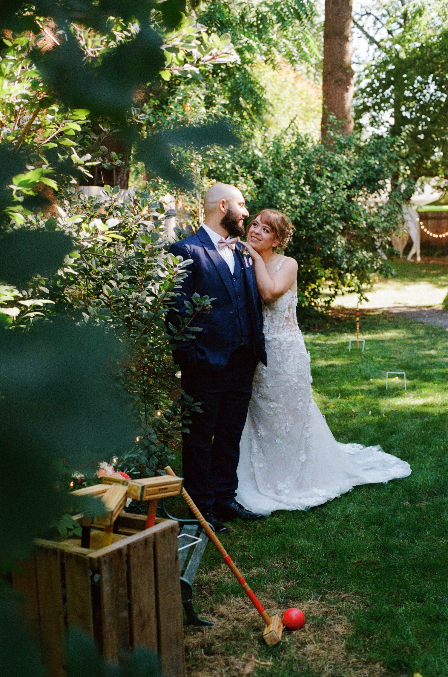 A romantic garden wedding moment with a white lace dress and navy suit against lush greenery and vintage wooden decor.