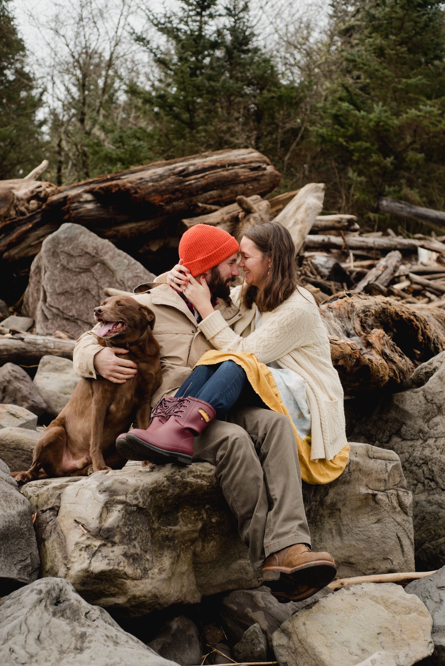 A romantic couple snuggling on rocky terrain with their dog beside them.