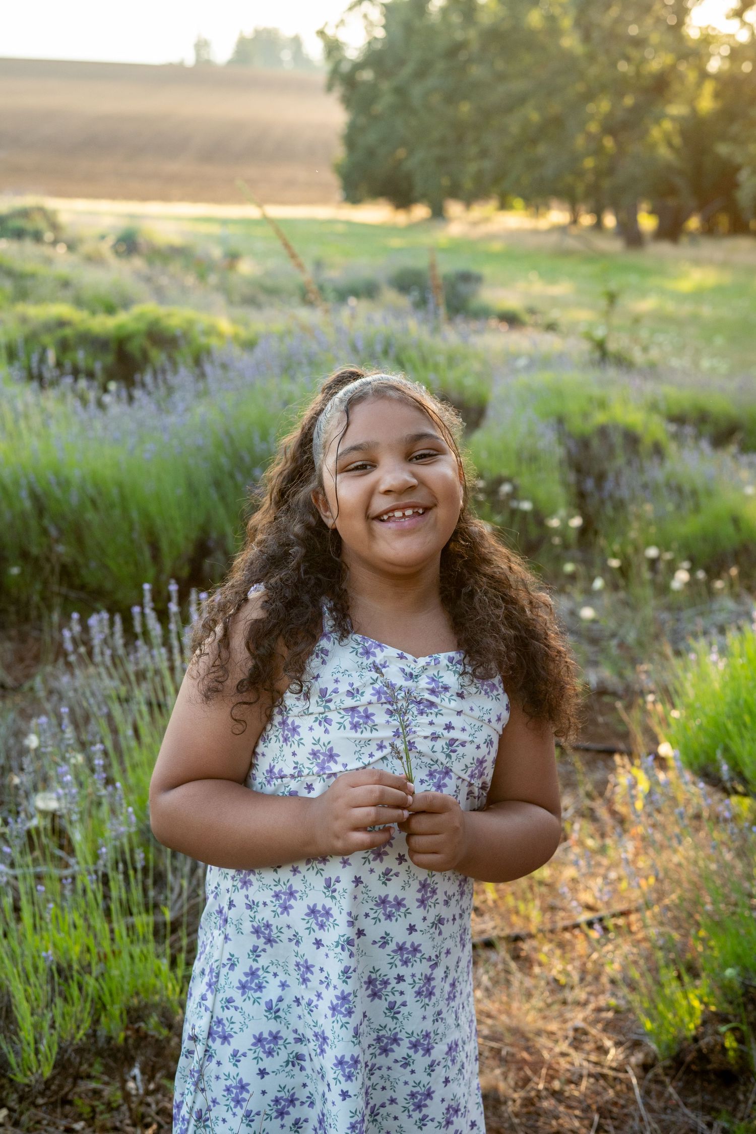 A young dancer twirls with joy in a floral dress surrounded by lavender flowers during a golden sunset.