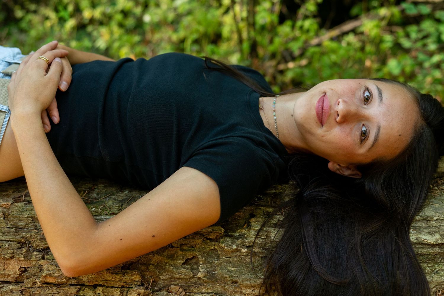 Person in black shirt laying down on rustic wooden surface outdoors with natural greenery in background.