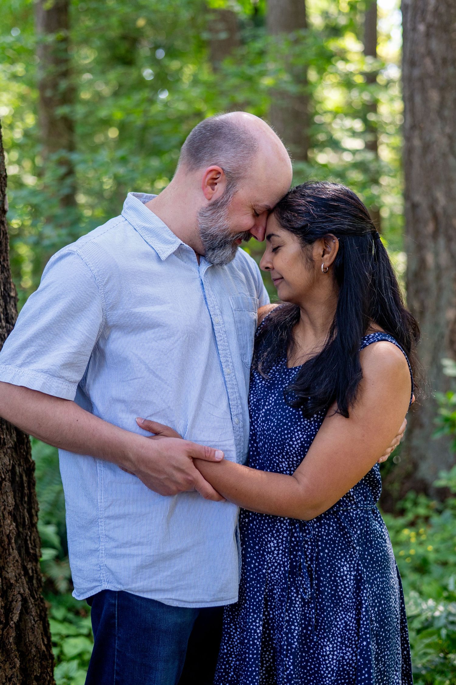 A couple shares intimate moments in a forest setting while wearing blue and white outfits.