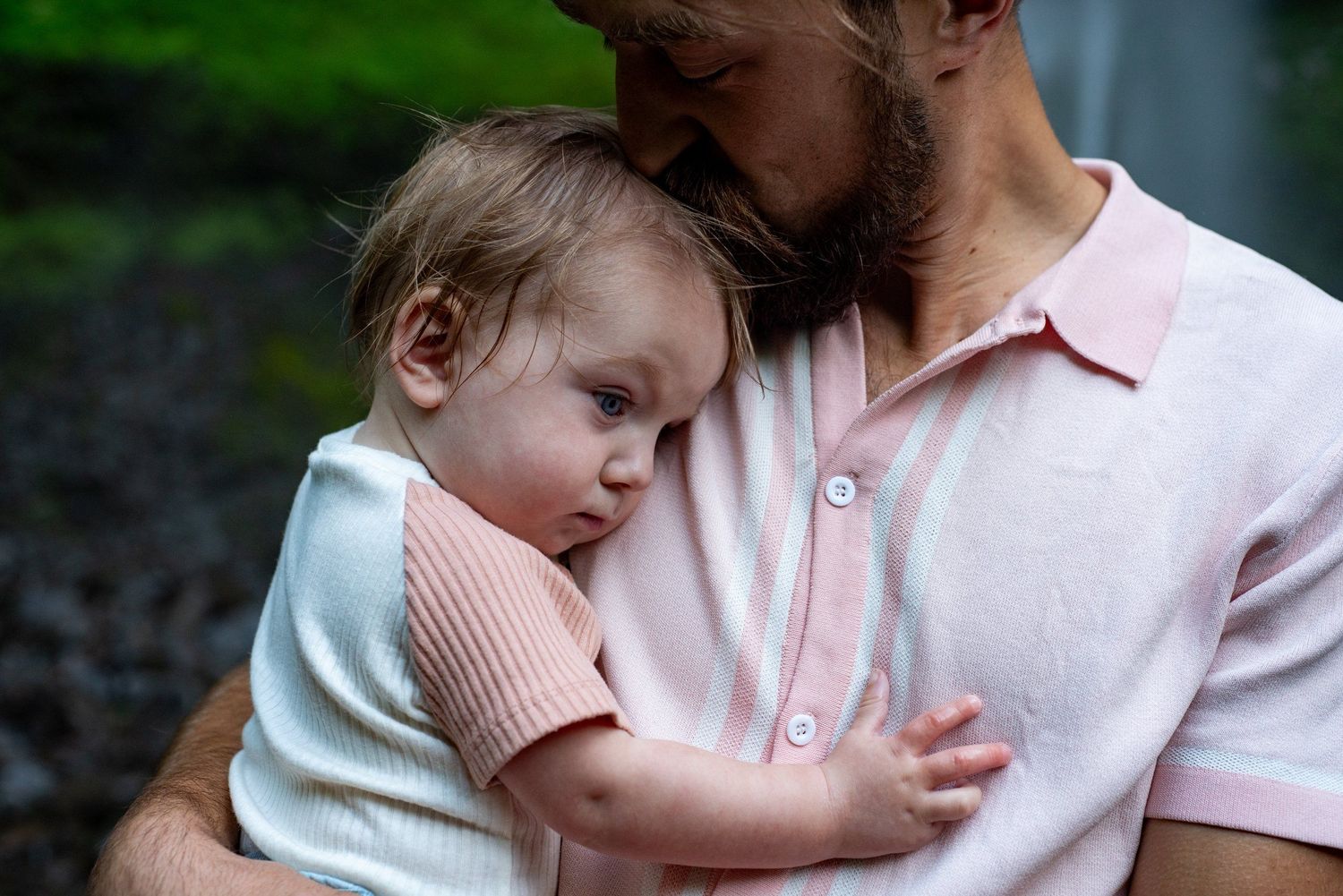 A small child rests peacefully against someone's shoulder in soft lighting.