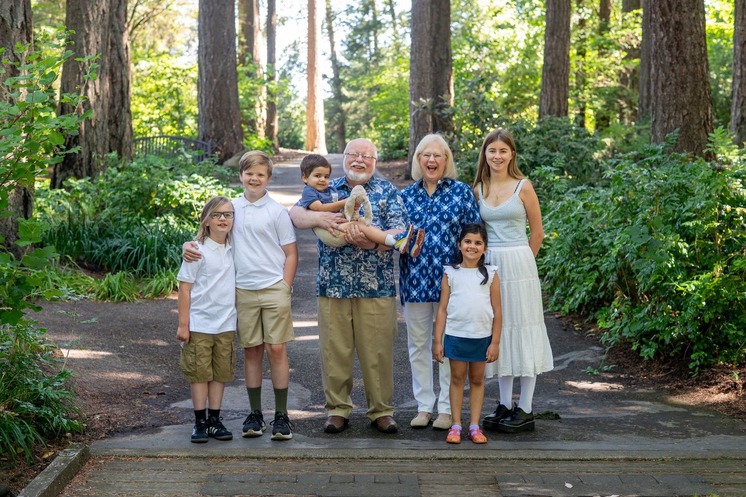 Family gathering on a forest trail surrounded by lush green trees and natural scenery on a bright sunny day.