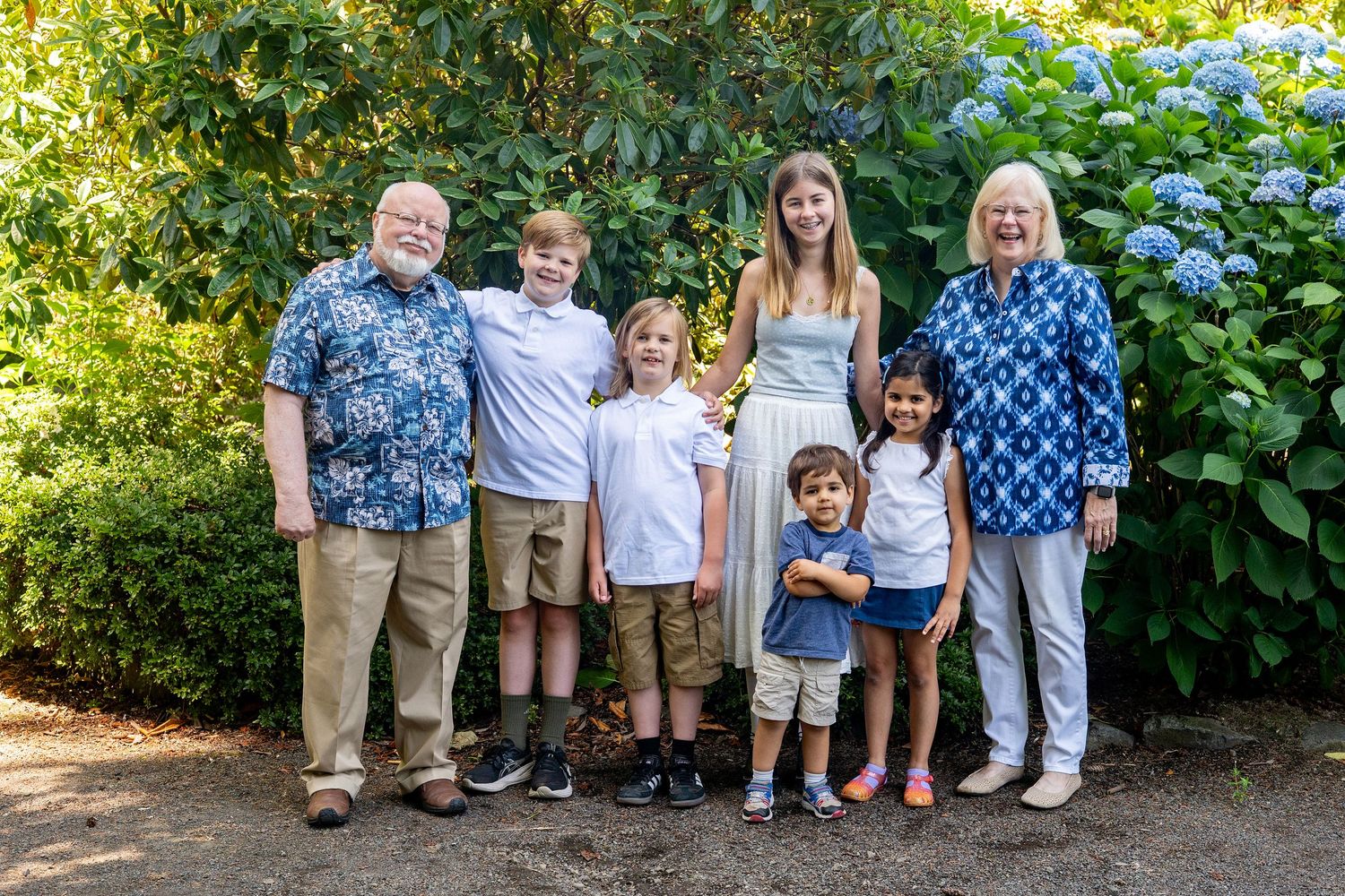 A group of people pose for family photos in front of blooming hydrangea bushes in a garden setting.