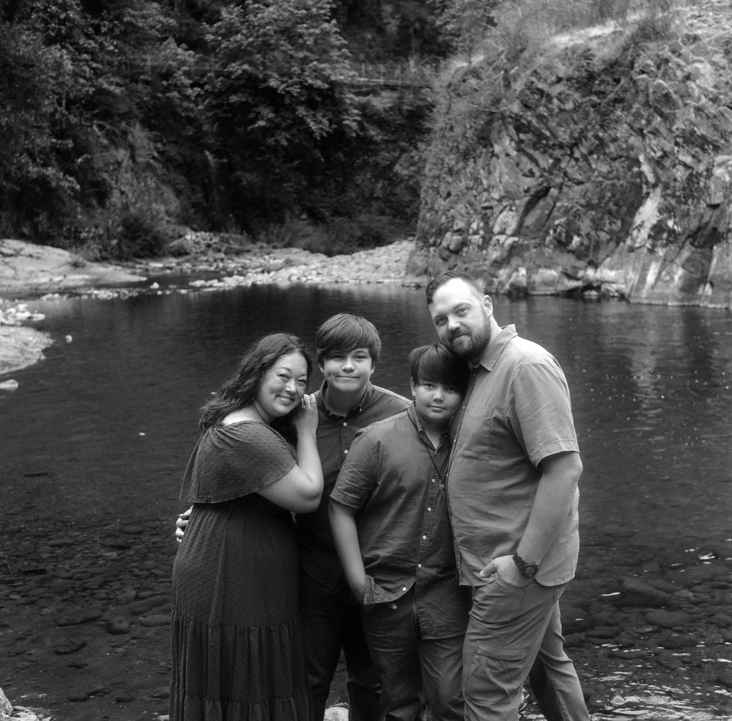 A group poses together by a scenic river surrounded by rocky cliffs.