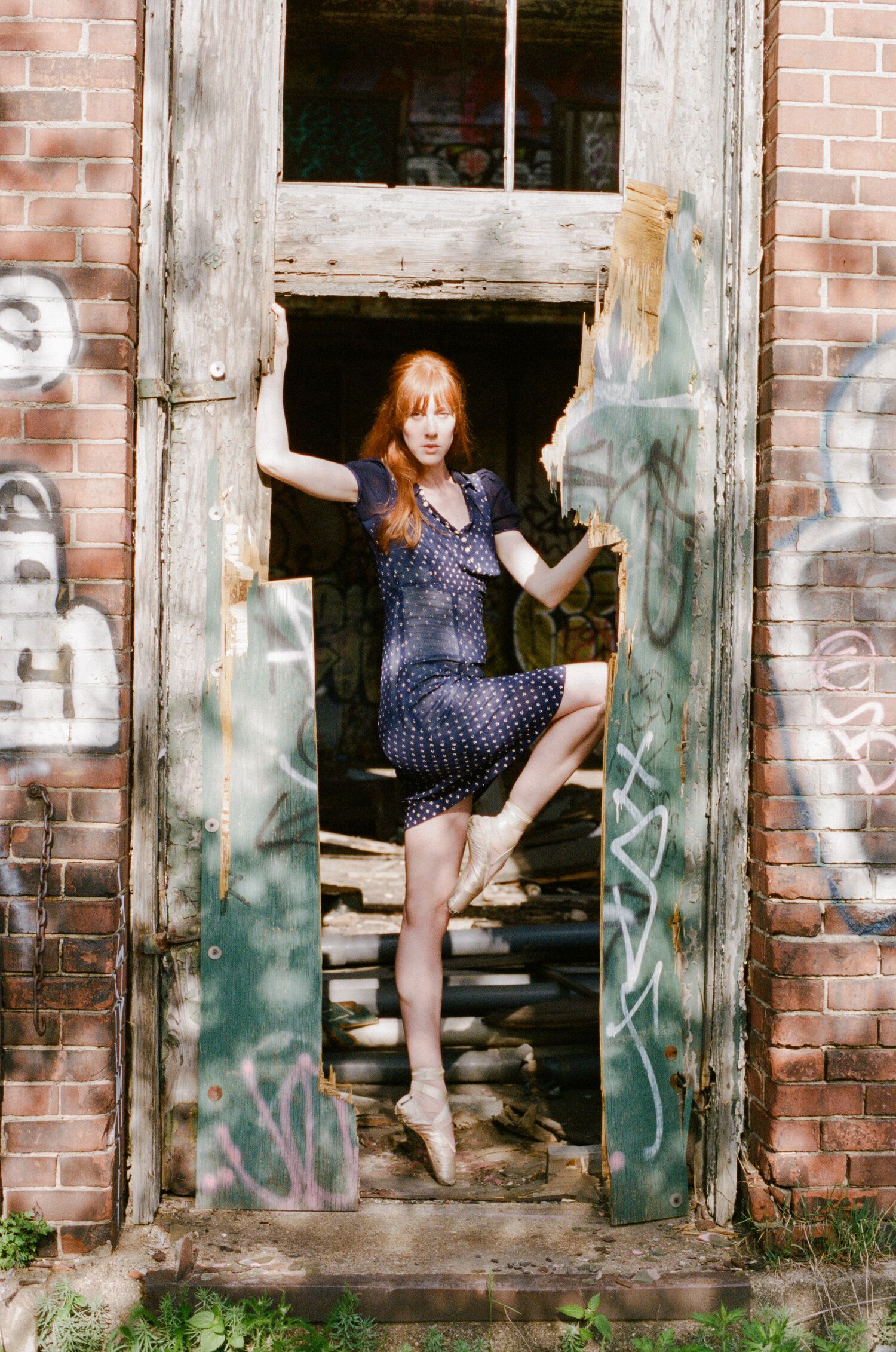 Ballet dancer strikes a graceful pose in a polka dot dress within a derelict doorway.