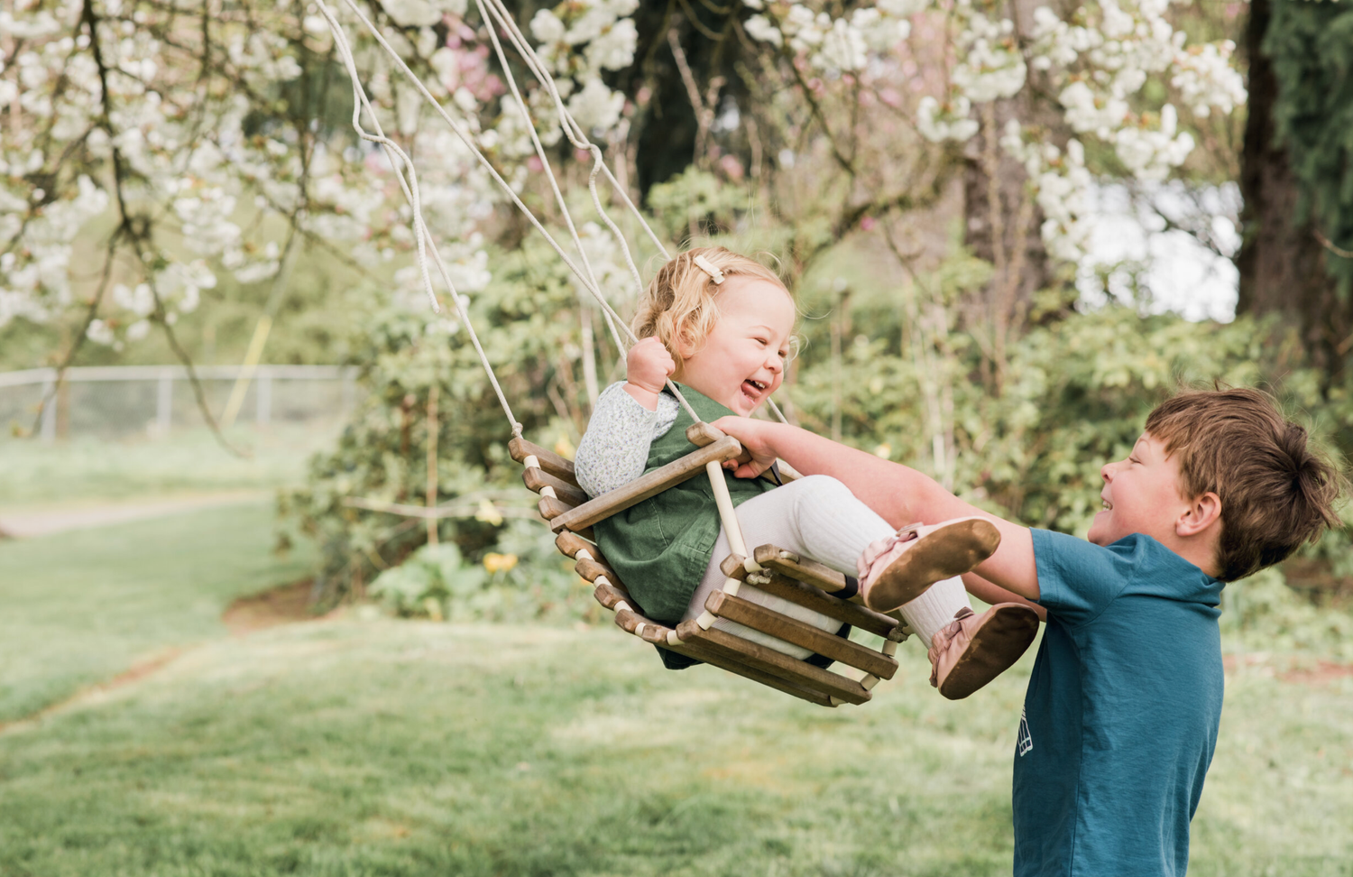Child being pushed on a swing by parent in a blooming spring garden.