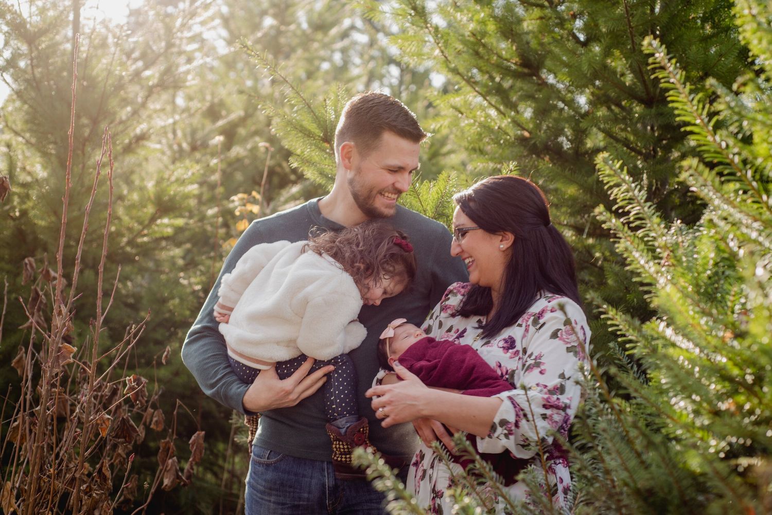 An intimate family moment outdoors among evergreen trees in soft sunlight.