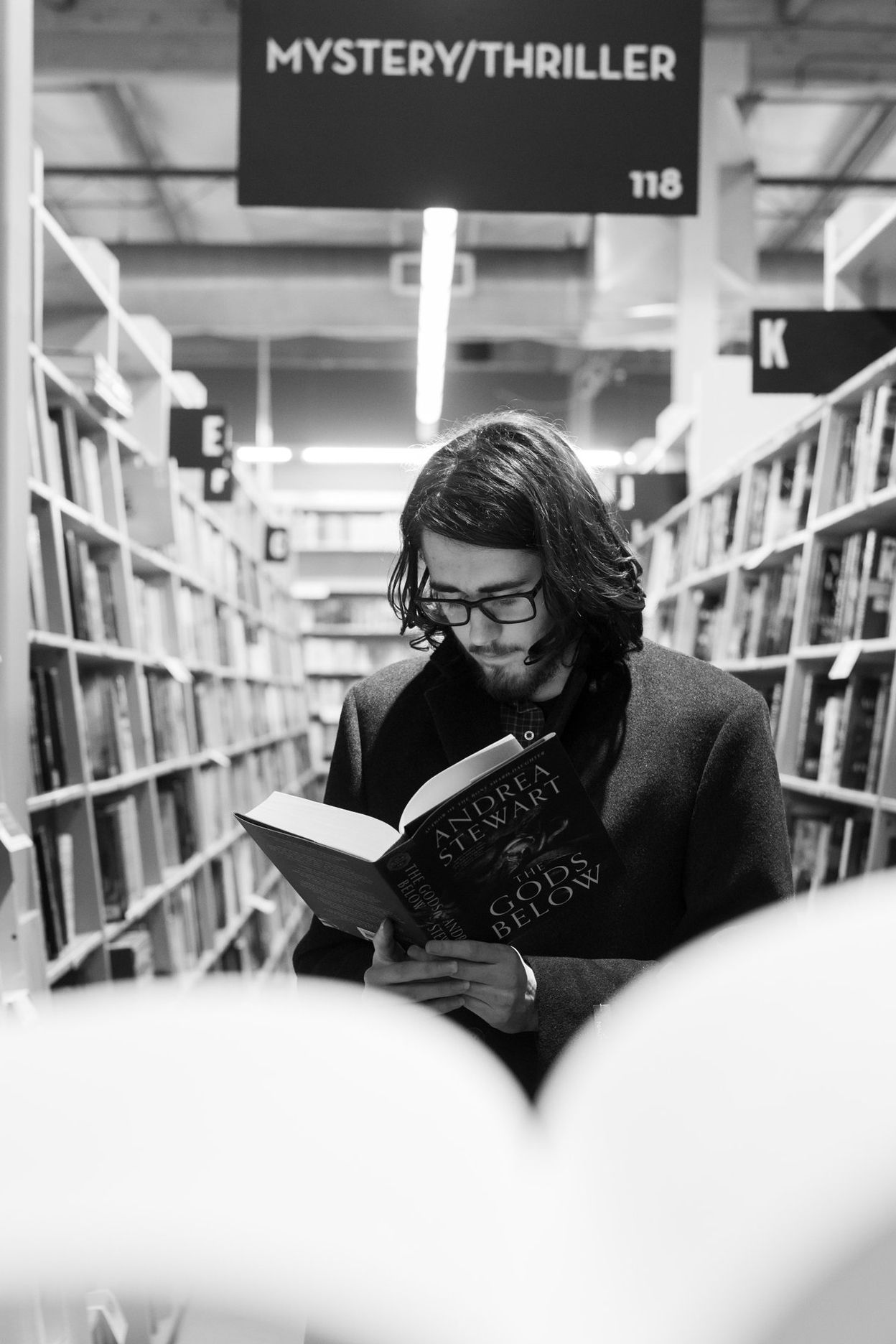 A person reads in the mystery and thriller section of a library or bookstore.