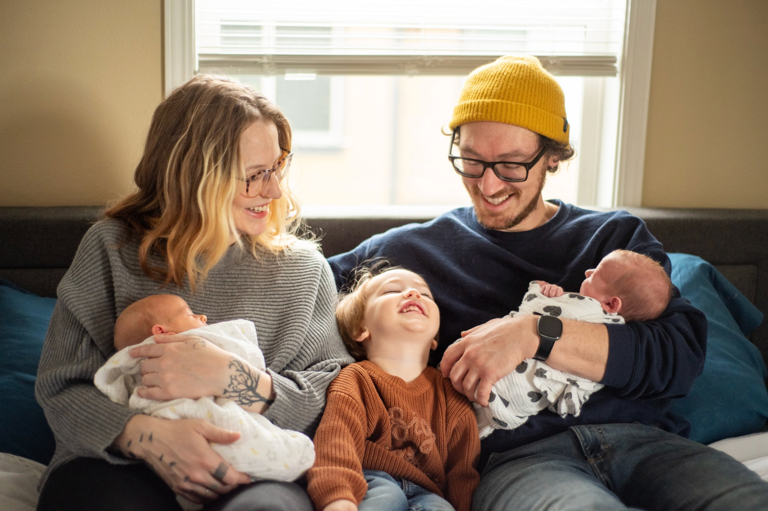 Family relaxing on couch with newborn twins and older sibling.