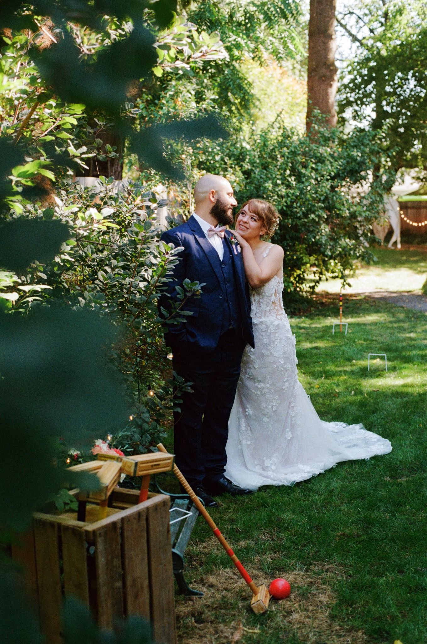 A wedding couple shares an intimate moment in a garden next to vintage croquet equipment.