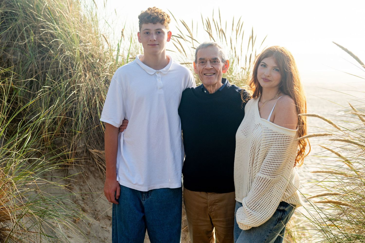 Group of people posing together on a beach with sand dunes and coastal grasses in the background.