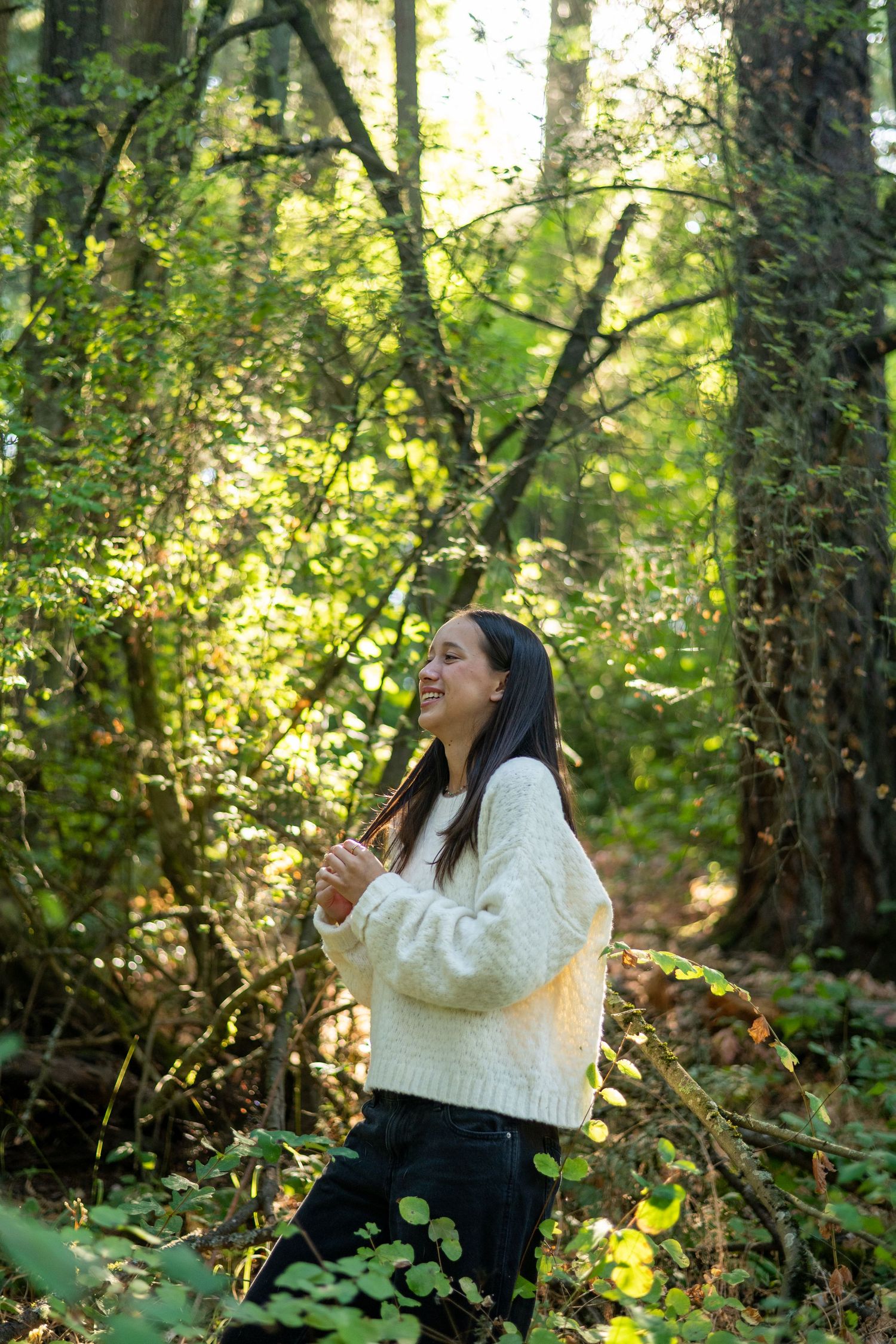 A series of photos shows someone sitting outdoors in a forest setting wearing a white sweater and laughing joyfully.