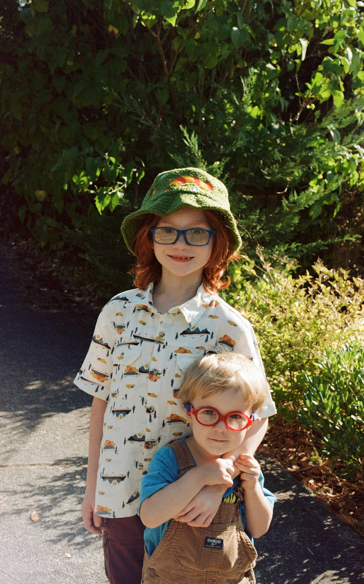 Two young children in summer attire standing together on sunny pathway.