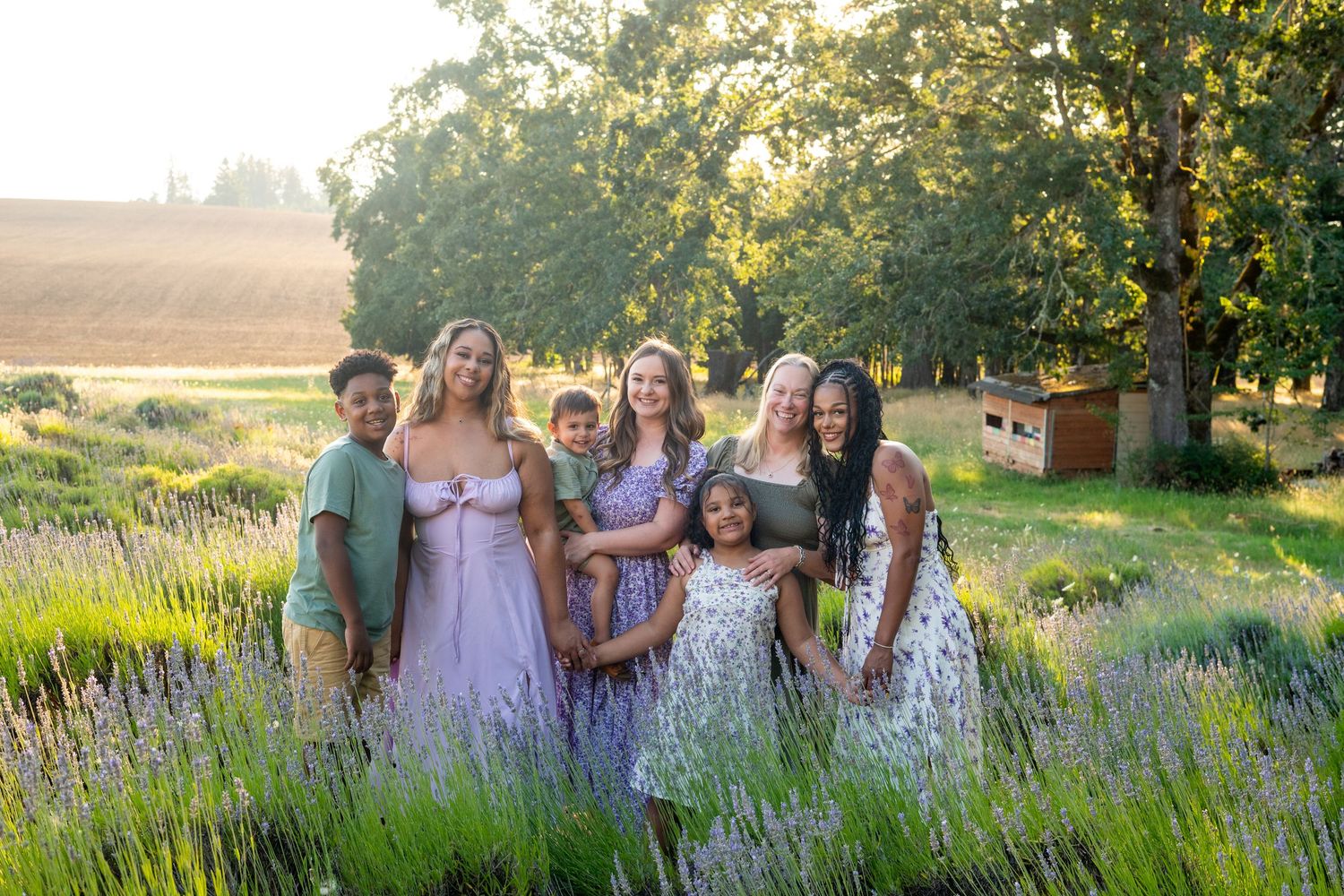 A group of people in coordinated pink and white outfits stand together in a sunlit garden with lavender flowers at sunset.