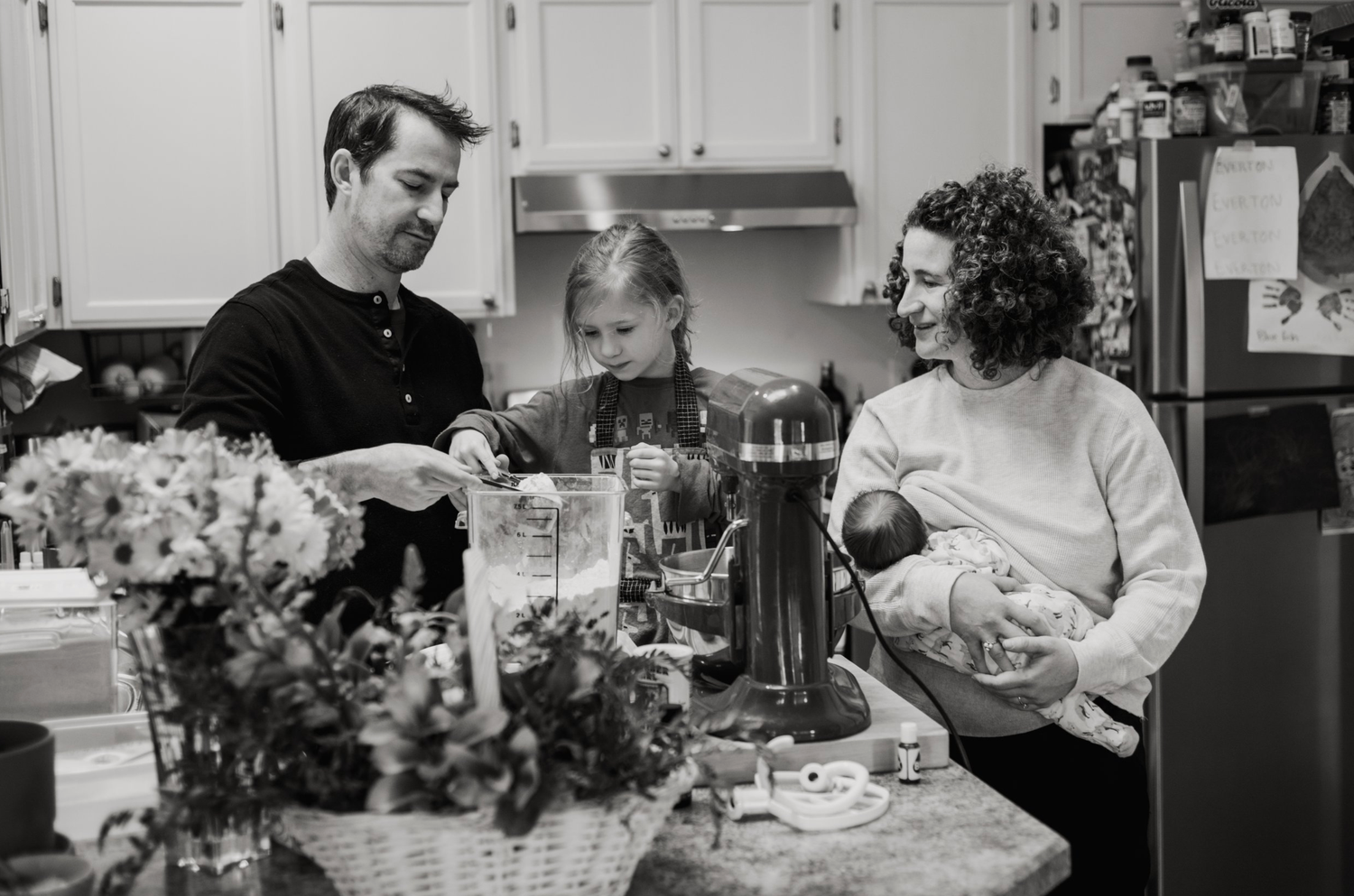 Family preparing food together in a cozy kitchen with flowers on the counter.