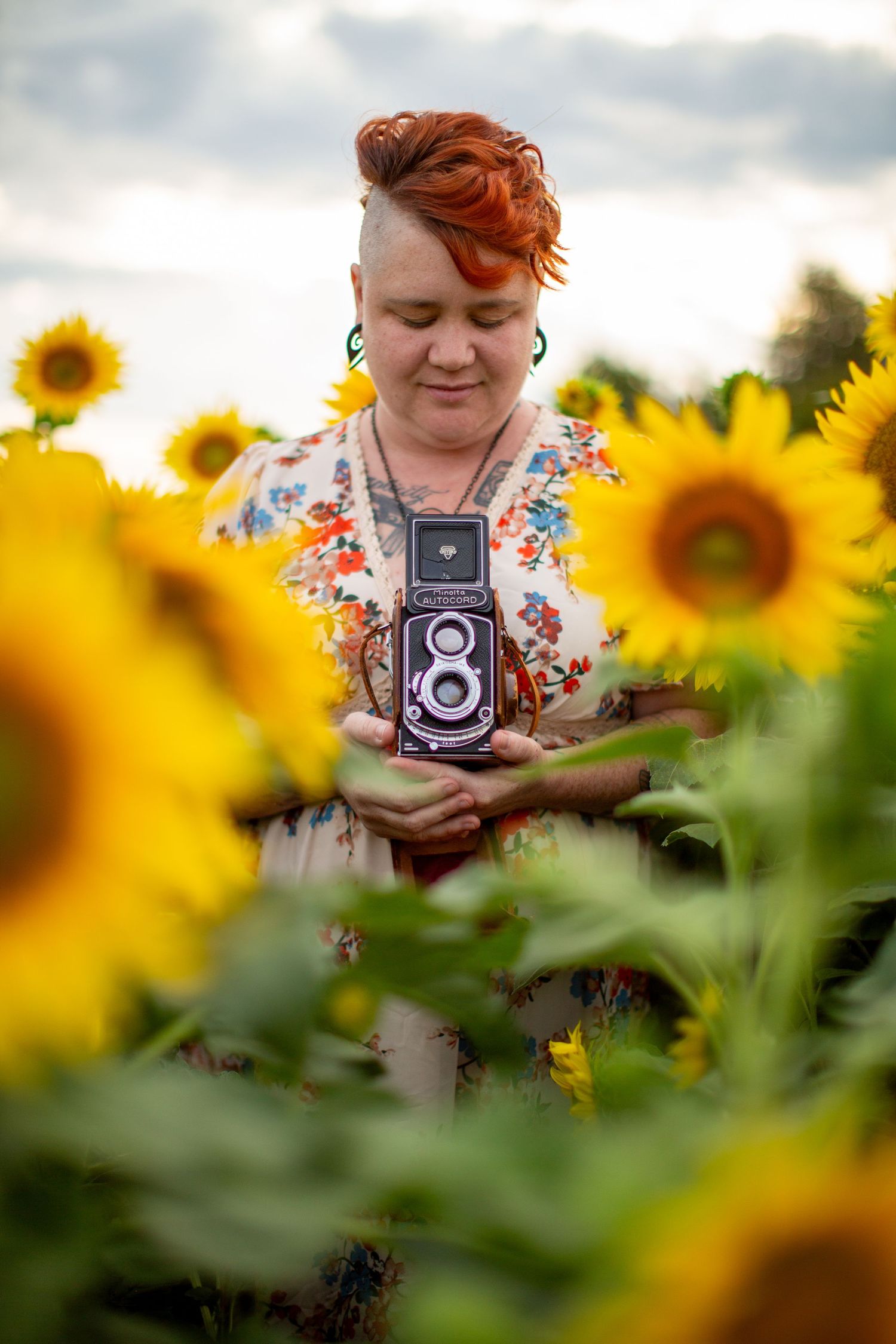 A photographer holding a vintage twin-lens camera amid blooming sunflowers in a golden summer field.